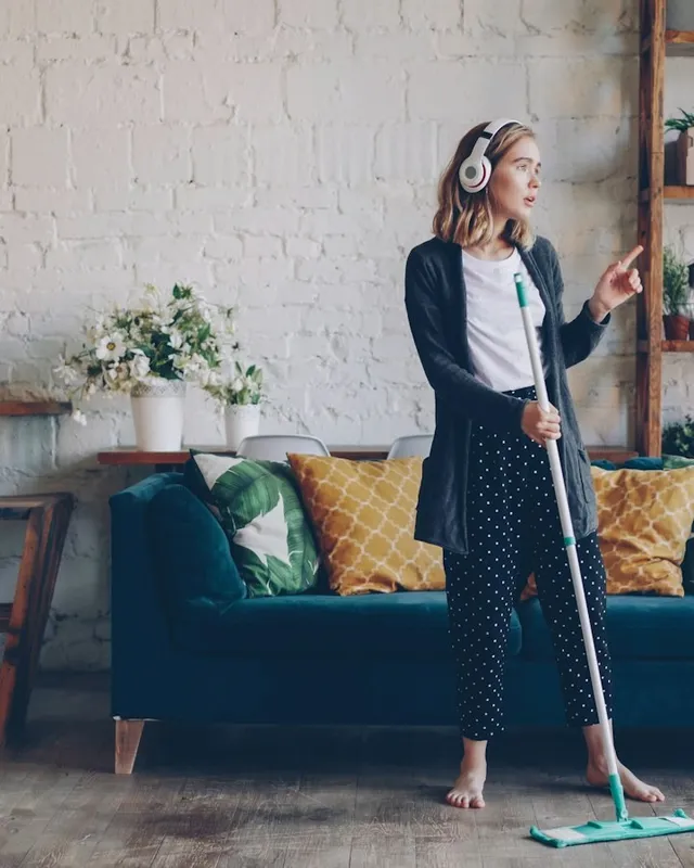 Woman in headphones mopping the floor of a bright living room