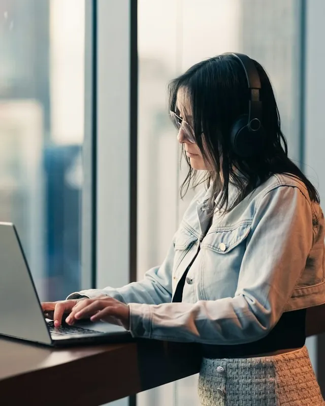Woman in headphones working on a laptop by a window