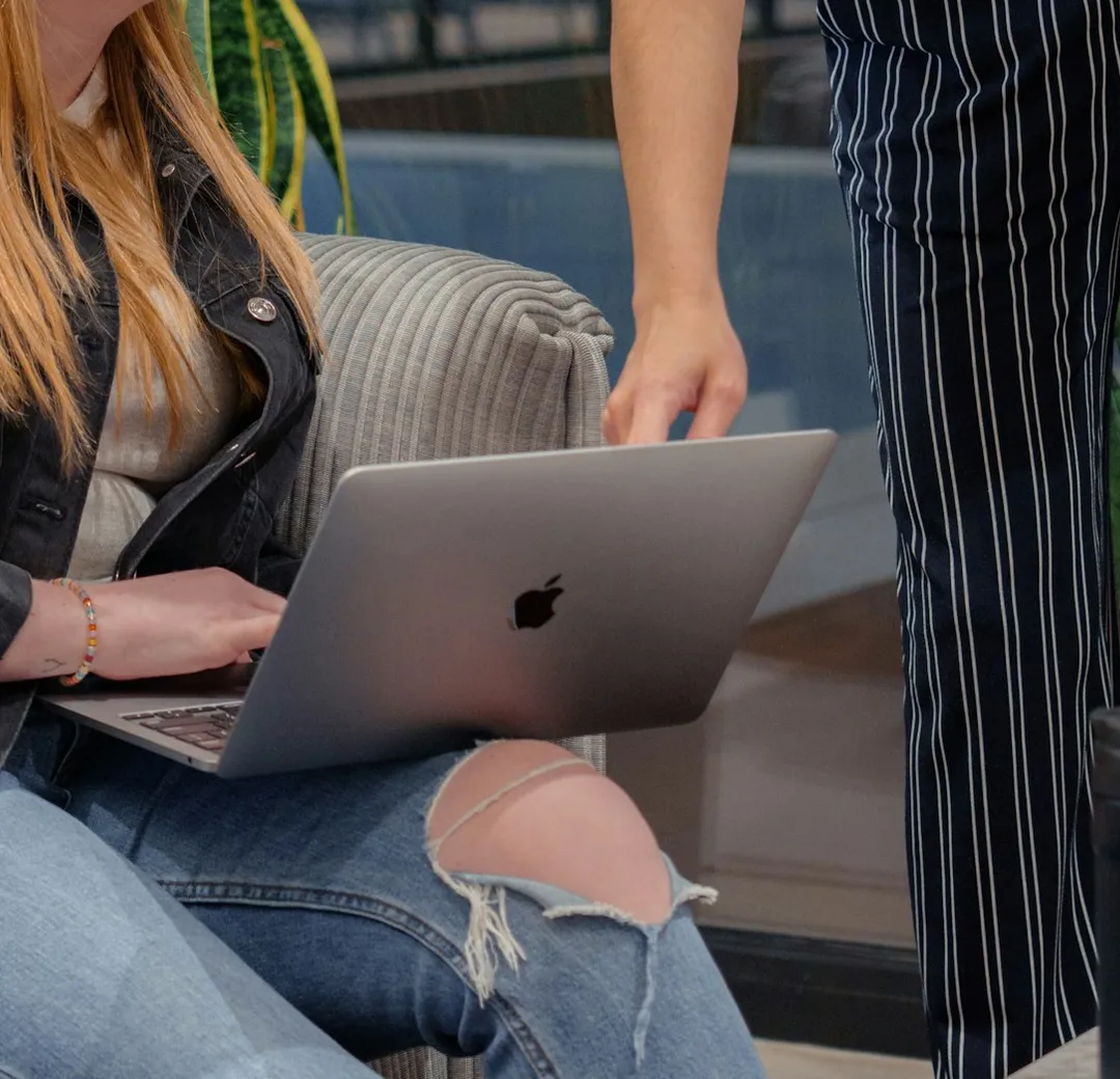 A teammate working on a laptop while a colleague points at the screen